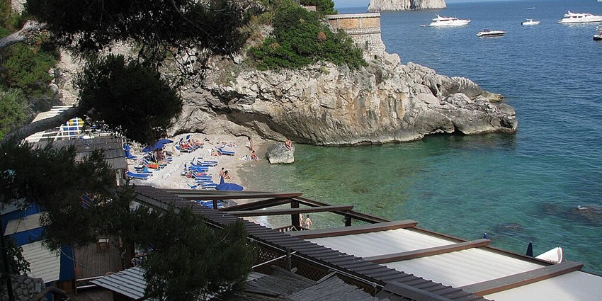 A scenic beach with clear waters and stunning Faraglioni views