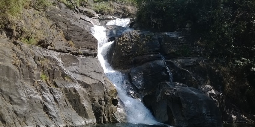 An image showing Meenmutty Waterfalls cascading down rocky terrain with greenery.
