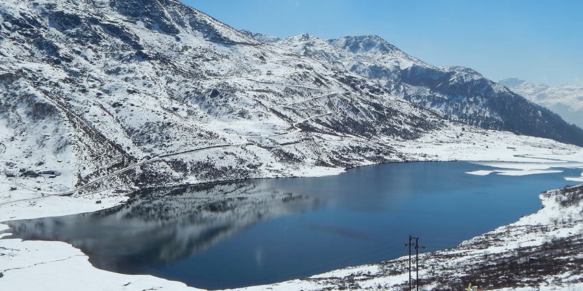Menmecho Lake surrounded by snowy land, mountains covered in snow reflecting on water.