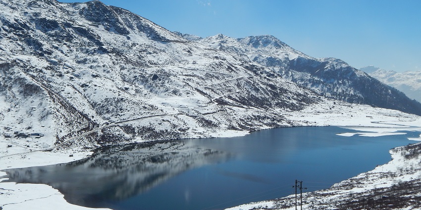 Menmecho Lake surrounded by bright white snow mountains and an electricity wire pole.
