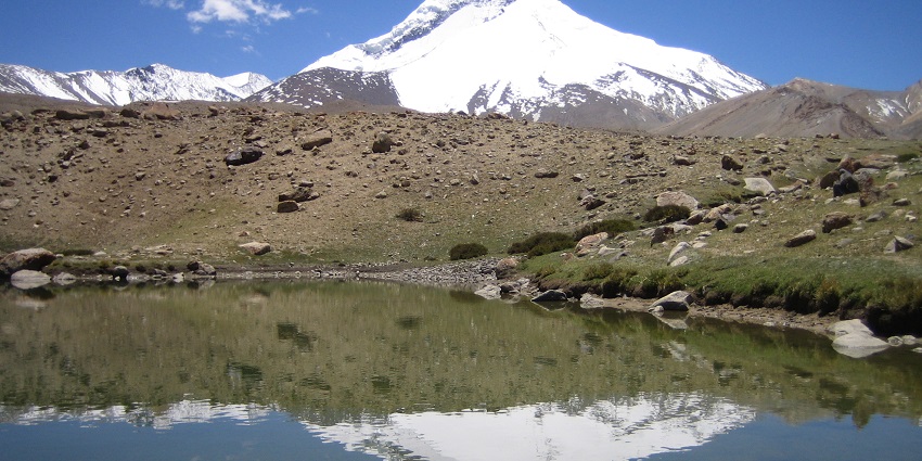 Lake with the reflection of distant snowy mountains, small rocks and sandy shoreline