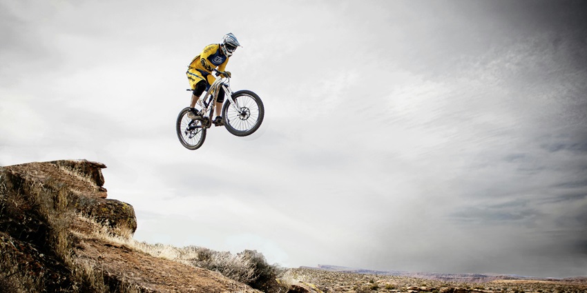A mountain biker in yellow gear and a helmet soars through the air after launching off