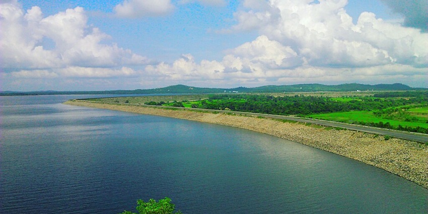 Mukutmanipur Dam Lake with sandy shores, a road parallel to the lake and greenery.