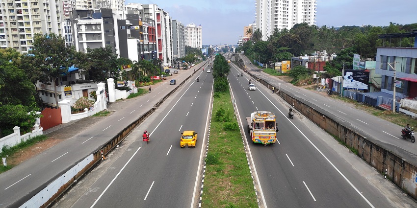 NH66 stretching between tall buildings and greenery, with cars and a truck driving