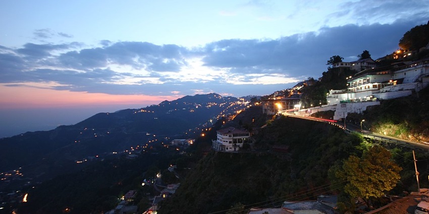 An image showing a serene evening at Mussoorie, with glowing lights and misty mountain views