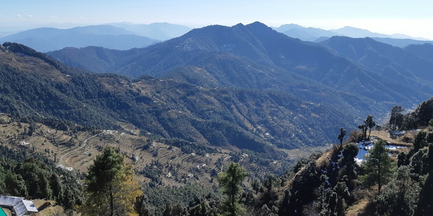An image of the hilly town of Mussoorie, with numerous buildings surrounded by trees and distant mountains