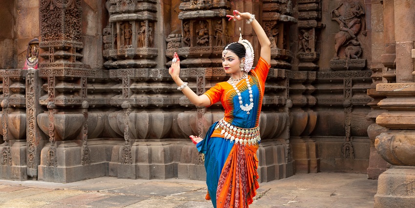 Indian classical dancer looks at the mirror during the dance recital against the backdrop of temple sculpture