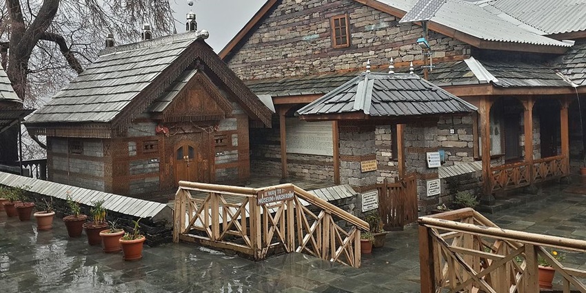 Naggar Castle courtyard with stone buildings, tiered roofs, and wooden balconies.