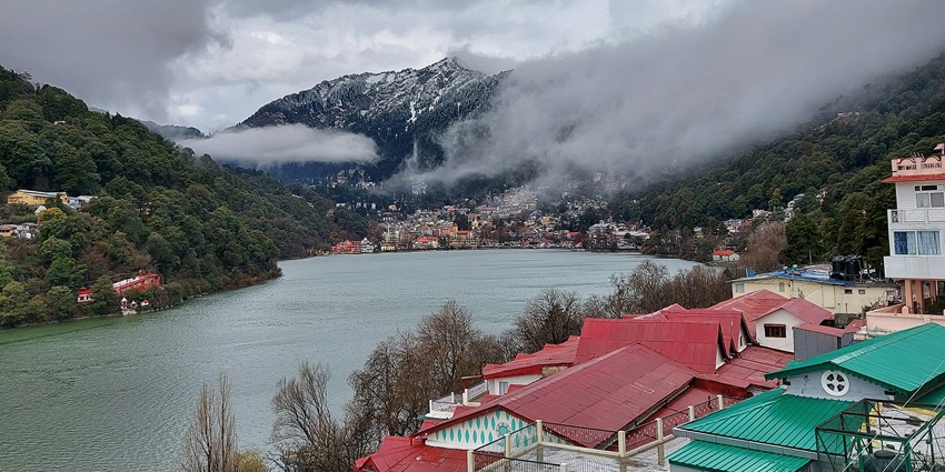Naini Lake in Nainital, surrounded by dense green hills with autumn reflections on the water.