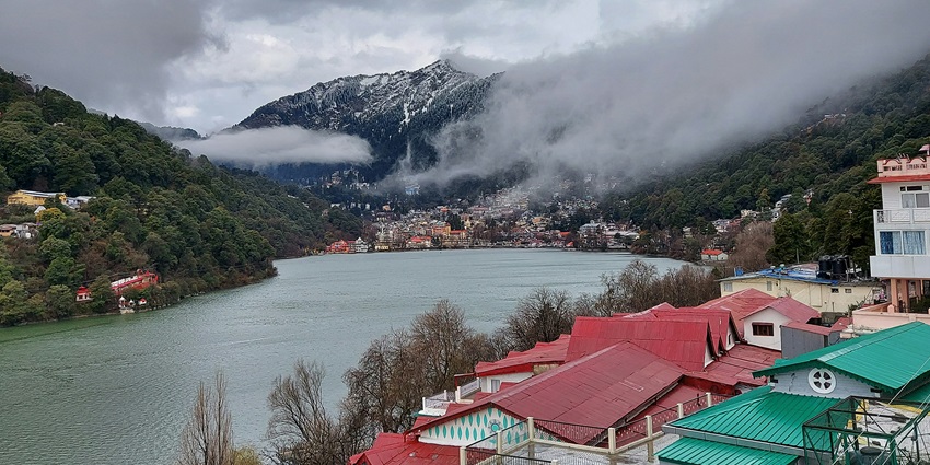An image of a calm lake in Nainital surrounded by green hills with boats on the water.