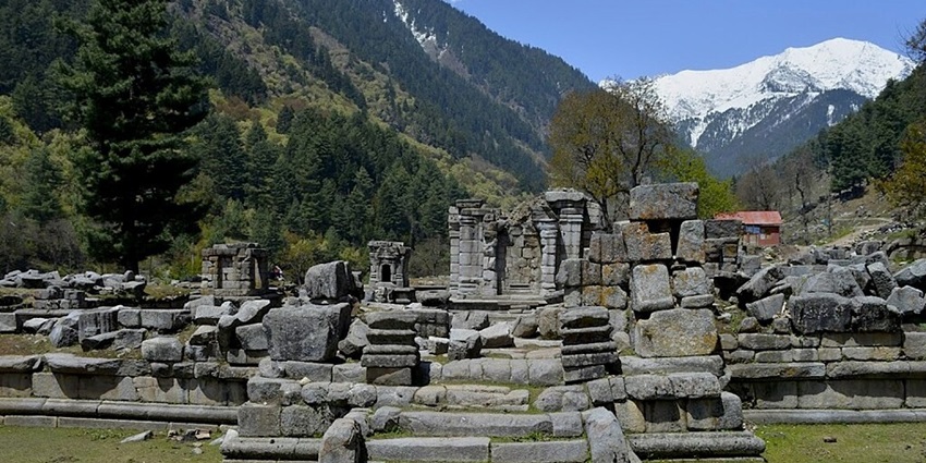 Ruins of Naranag temple with grey broken stones everywhere and distant snow mountains.