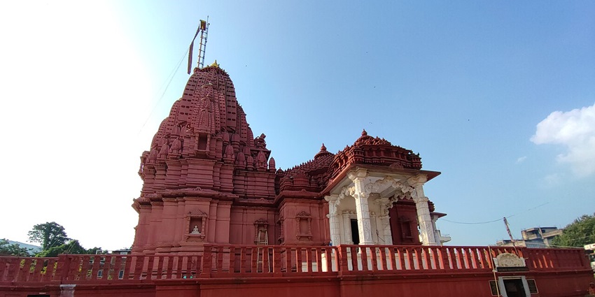 An image of Naulakha Jain temple with the red architecture, entrance gate and two statues