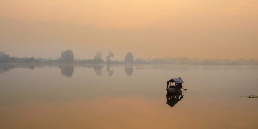 An image of Nigeen Lake at sunrise with golden hues, calm waters, and a peaceful atmosphere.