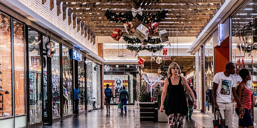 An image of a shopping mall decorated with Christmas ornaments, including gift boxes and wreaths, with shoppers.