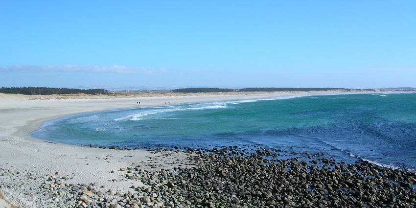 An image of Orrestranda Beach, where clear waters meet a sandy shore under a sunny sky.