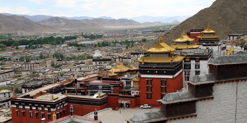 A view of Shigatse Monastery with its red and gold buildings, set against a mountainous backdrop