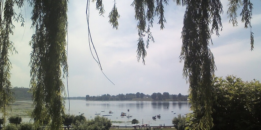 Manasbal Lake with vehicles parked near Manasbal Lake in Kashmir and boats rowing in the lake.