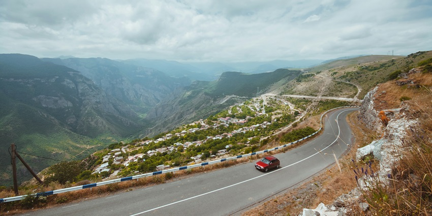 a red car driving to the mountains - unveiling both beautiful architecture of the Tatev Monastery