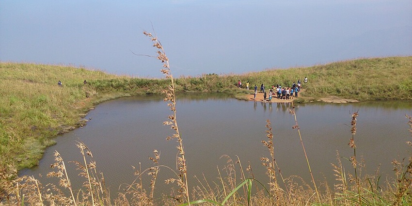 Chembra Lake, the heart shaped lake in India, has green shorelines with a crowd of people.