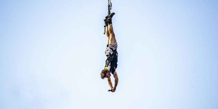 Snapshot of a man upside down hanging from the rope for Bungee Jumping