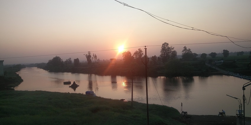 Panchaganga River with electricity wire poles and a bright sunset in the background