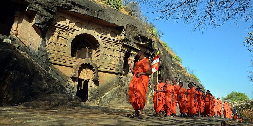 Buddhist monks in orange robes standing by rock-cut Pandavleni Cave entrance near Nashik