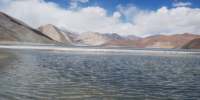 An image of Pangong Lake at high altitude, surrounded by rugged mountains and clear water.