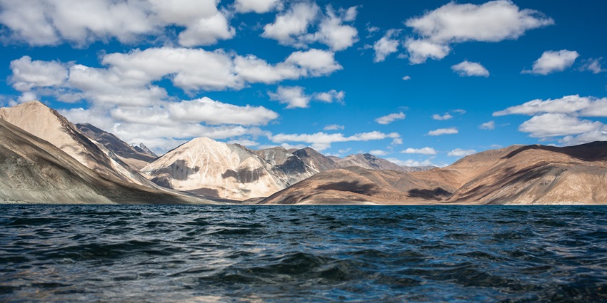 An image of a Scenic view of Pangong Tso Lake with clear blue water and surrounding mountains.