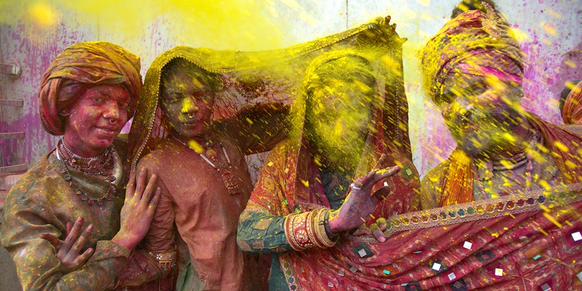 A group of women pose for a photo while yellow gulal showers over them during Holi