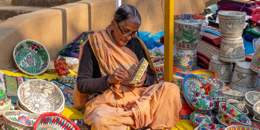 A woman wearing a traditional saree painting handmade pottery items at Surajkund Mela.