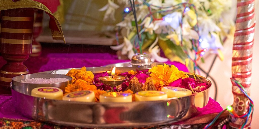 A traditional Hindu pooja thali with a diya, flowers, incense, and sacred offerings
