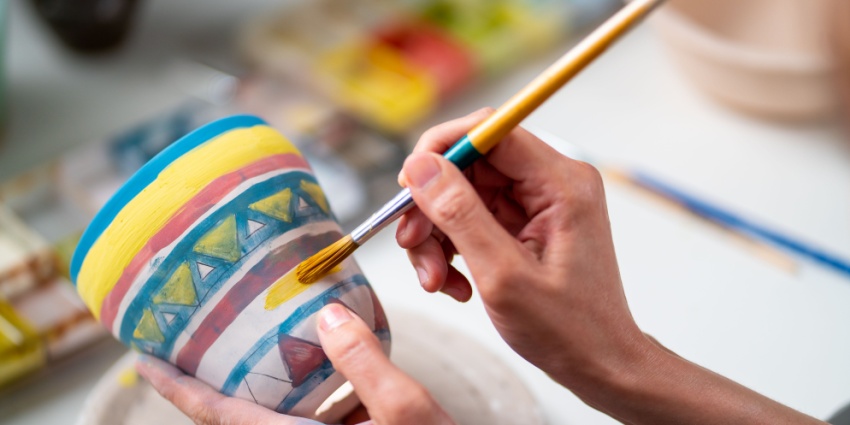 An image of an Asian woman learning colour painting self-made pottery at a workshop.