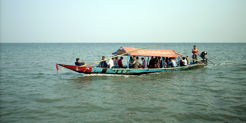 Several people riding a boat and passing against the gentle waves of Chilika Lake