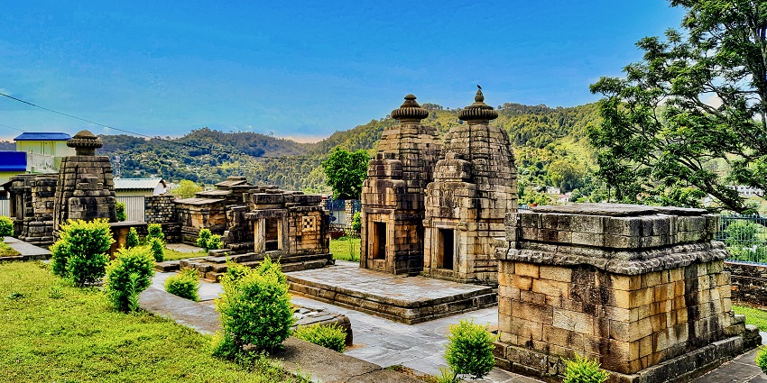 View of Patal Bhuvaneshwar Temple, surrounded by lush gardens and blue sky in the background