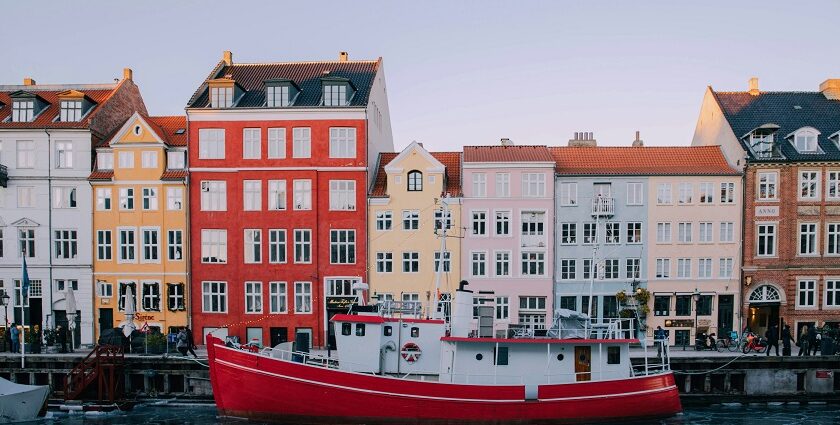 An image of colourful buildings along a canal in Denmark, with boats and pedestrians.