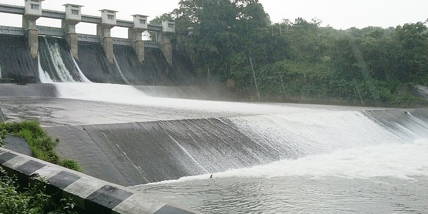 Water flowing through the dam with concrete architecture and dense greenery around it