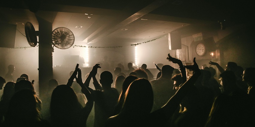 A crowded nightclub in Pune, with people dancing and raising their hands under dim lighting.