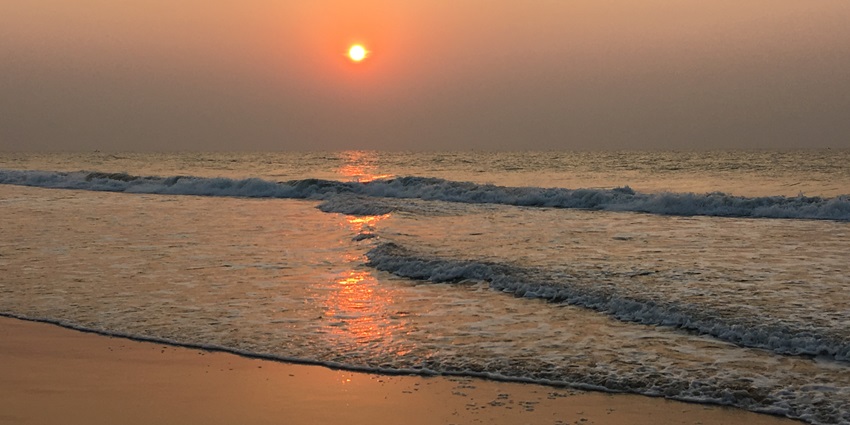 A sunrise at Puri Beach with the sun rising over the horizon and reflecting on the water.