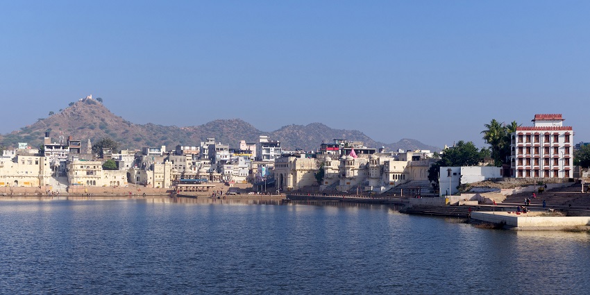 Pushkar Lake with stairs leading to the lake, multiple buildings and mountains in the back