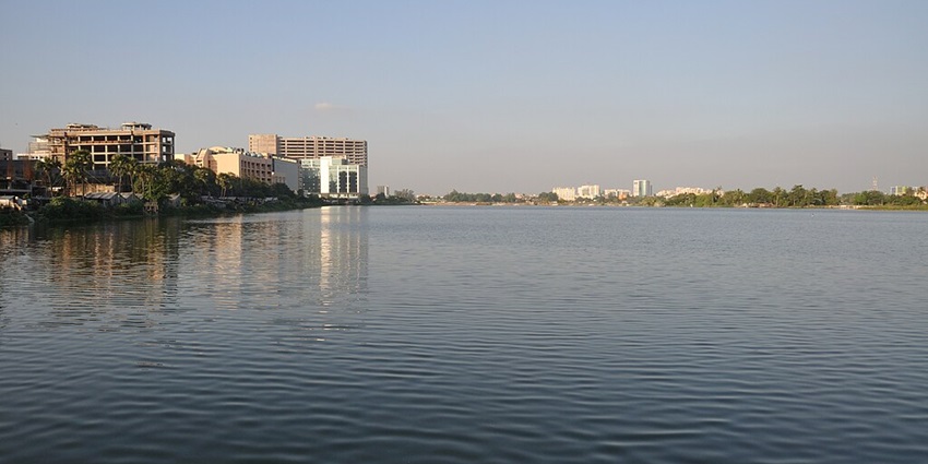 Lake with a still water body, green shores, buildings and green trees near the lake.