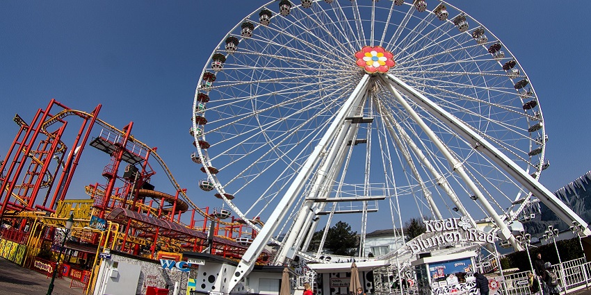 An image of the entrance of a theme park with sights of a giant wheel and other rides.