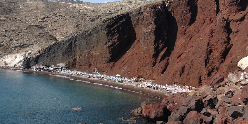 Scenic view of Santorini red beach around red rock hills and clear blue water
