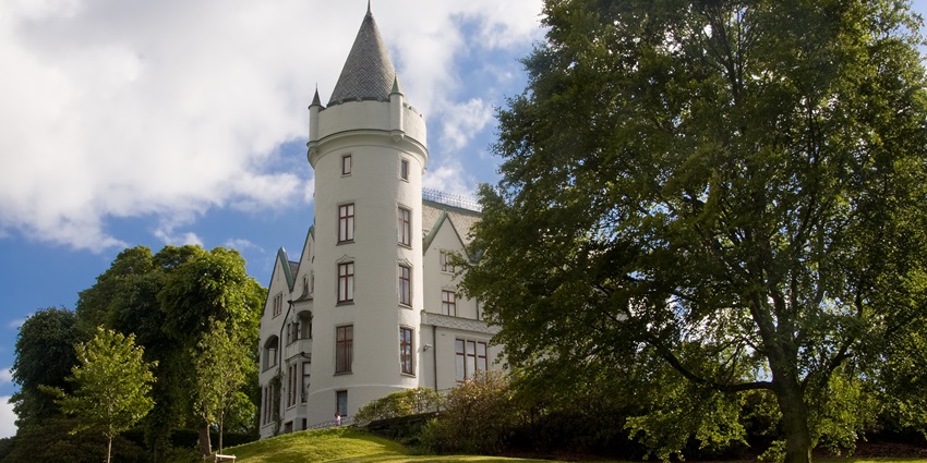 An Image of the Gamlehaugen, with trees and greenery surrounding the tower building.