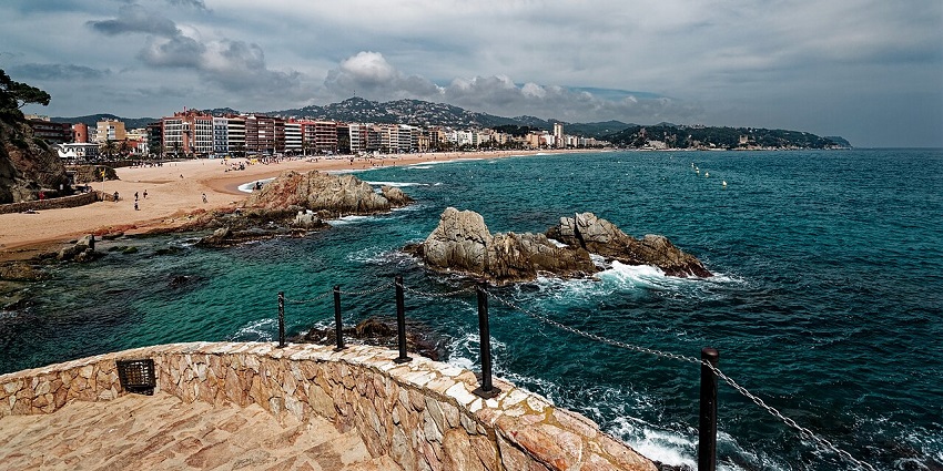 A tranquil cove on Costa Brava with turquoise waters, golden sand, and pine-covered cliffs, one of the best things to see in Spain in September.
