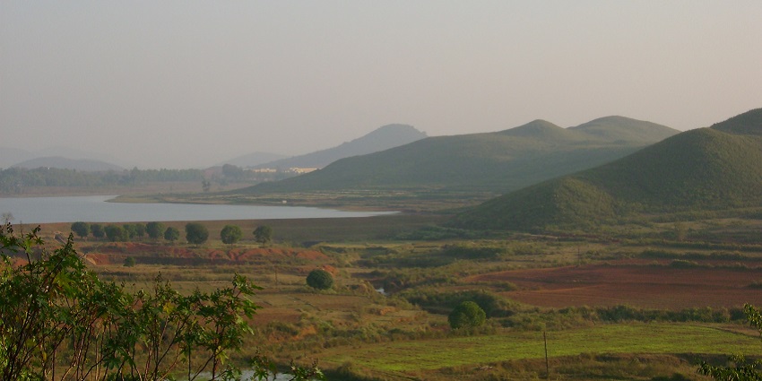 Dam reservoir with a large waterbody, greeny shorelines and mountains in the back