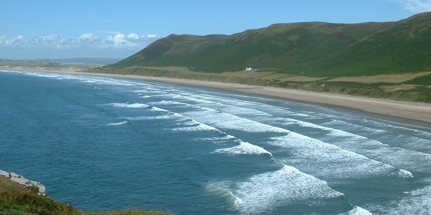 A vast and breathtaking Rhossili Bay, a sandy beach with rolling waves in Wales.