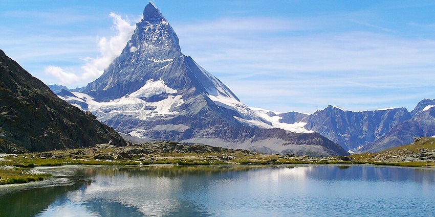 An image view of Riffelsee in Switzerland with clear waters reflecting the Matterhorn and a scenic alpine landscape