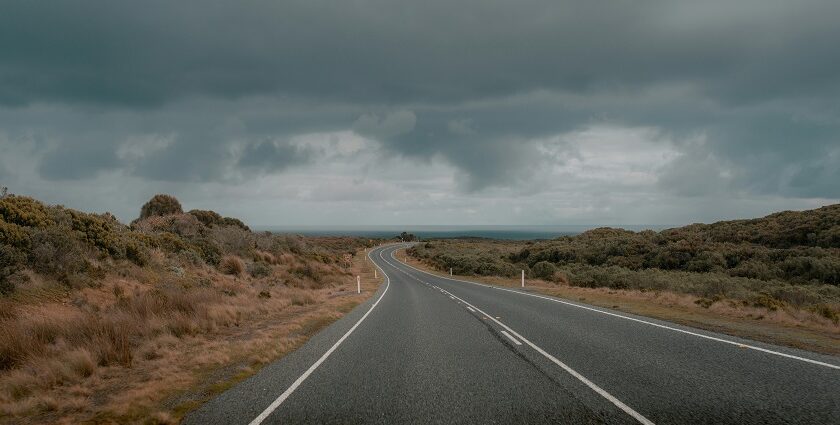 A dark road curves into the distance under a stormy sky similar to road trips in India