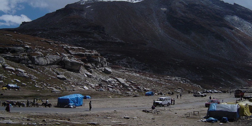 Image of Rohtang pass with a road and trekkers against a backdrop of snow-capped mountains