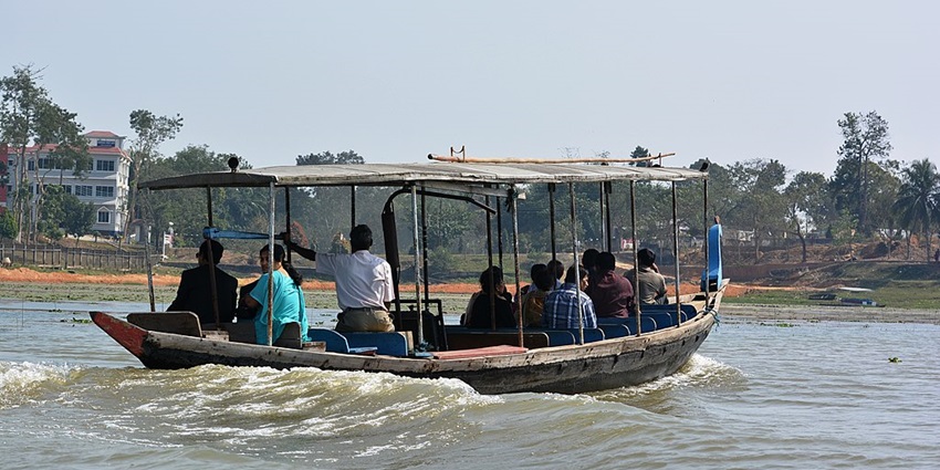 Rudrasagar Lake with multiple people sitting inside a boat and buildings in the back